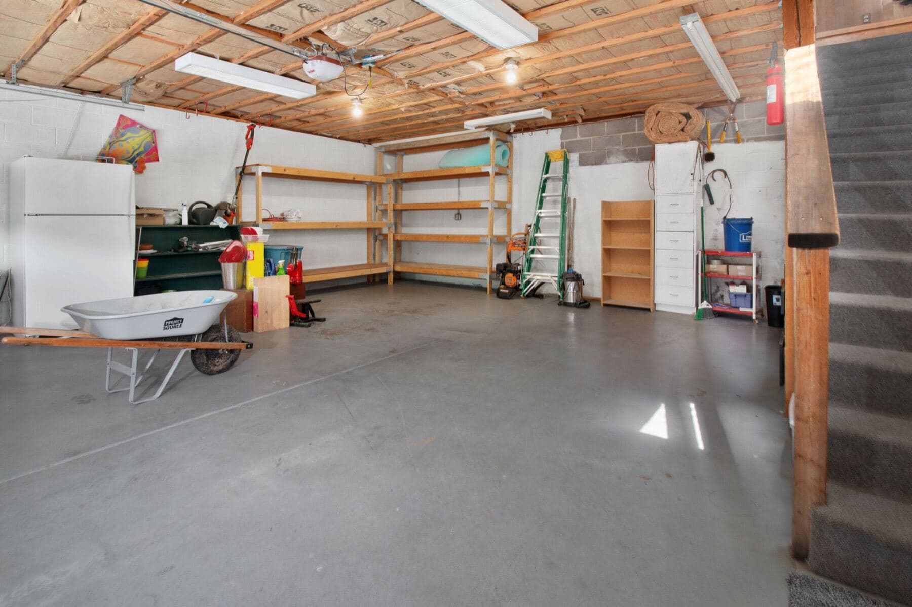 A home garage with bare concrete underfoot, shelving and stored tools.