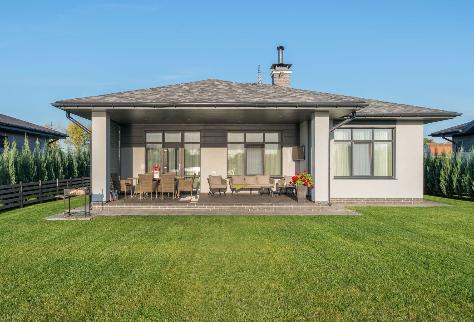 A residential backyard with a wide concrete patio running along the back of the house.